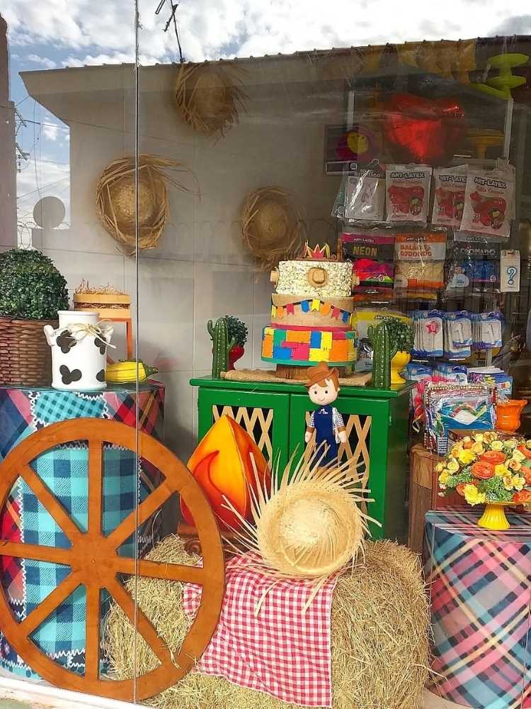 Vitrine de festa junina com caixas xadrez, chapéus de palha e feno 
