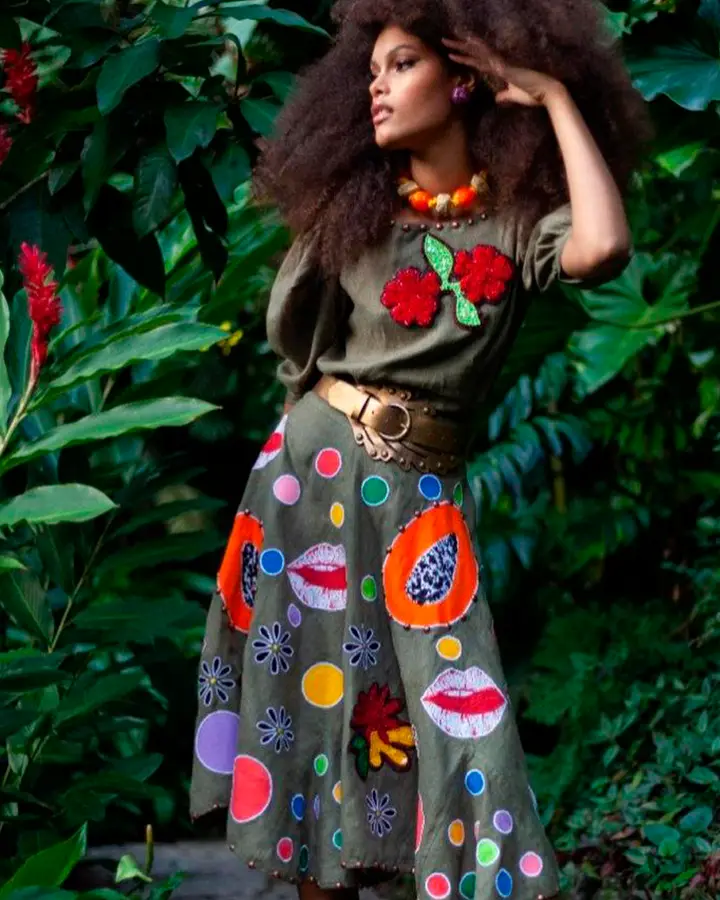 Modelo usa vestido verde com bordados diversos e coloridos.