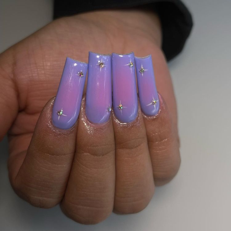 Pessoa de pele morena com unhas aura nails em roxo, com pedraria prata