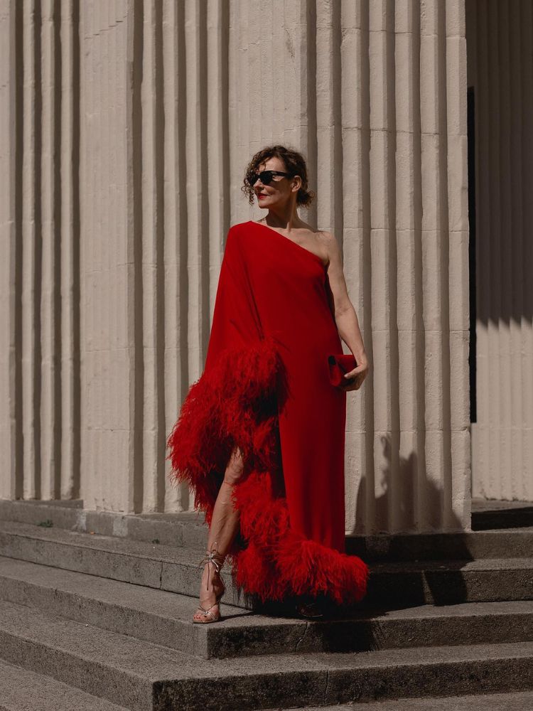 Senhora de pele clara usando vestido vermelho fluido com ombro só e manga de pluma 