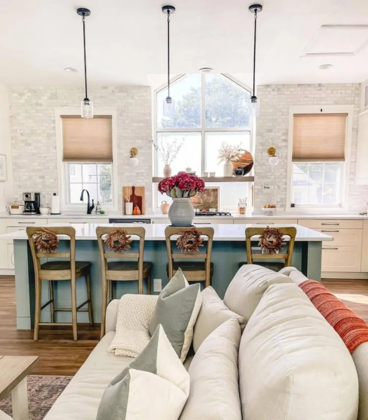 Sala integrada com cozinha com ilha azul, cadeiras vintage, parede de tijolos à vista, sofá off-white