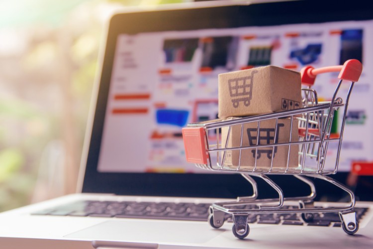 Foto de computador aberto em site de compras com carrinho de brinquedo ao lado 