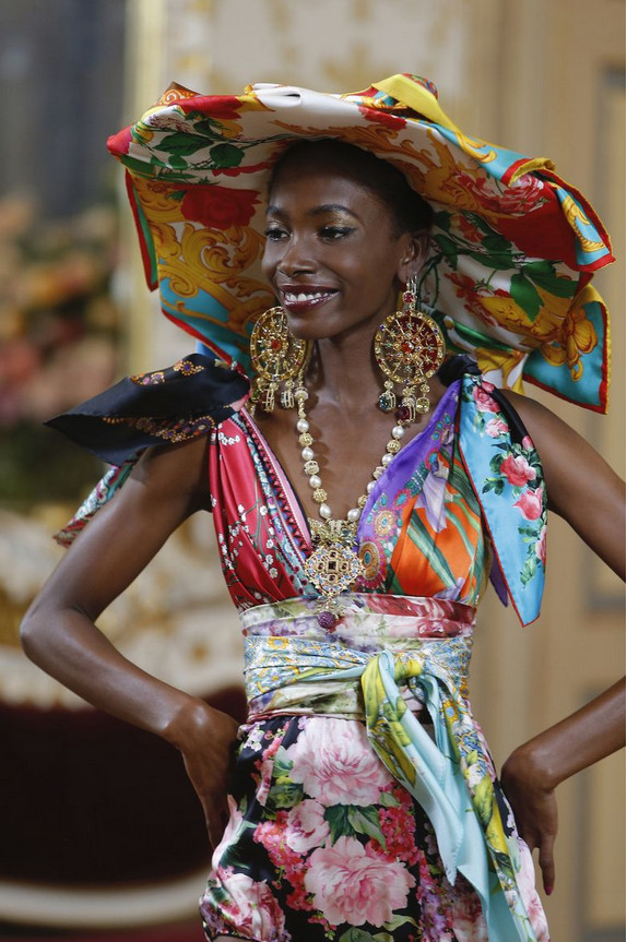 Modelo negra usando chapéu e maxi brincos com colar usando vestido feito de lenços com estampas variadas Modelo negra usando chapéu e maxi brincos com colar