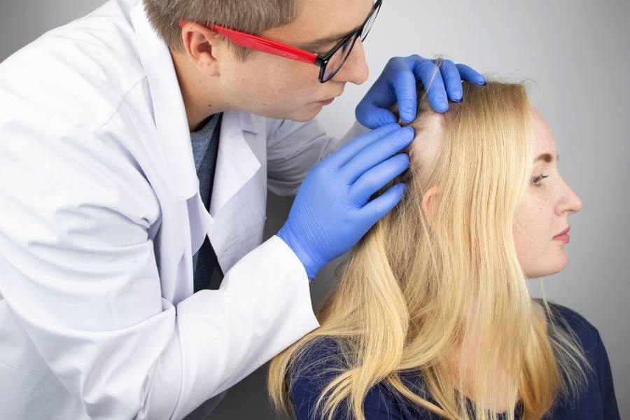 Médico avaliando queda de cabelo de mulher loira.