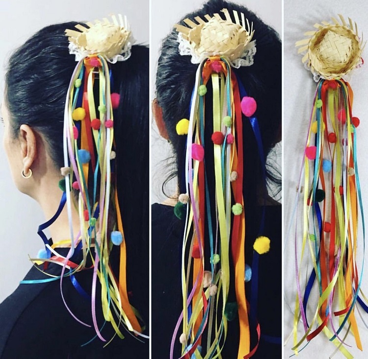 Mulher de cabelo preto usando adereço de festa junina com chapéu de palha, fitas coloridas e pompons
