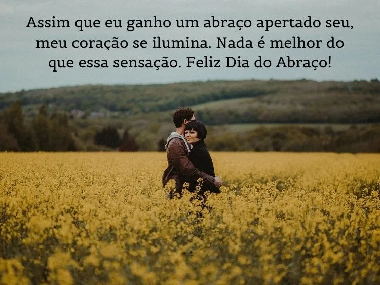 Foto de homem e mulher se abraçando no meio de flores e frase:  Assim que eu ganho um abraço apertado seu, meu coração se ilumina. Nada é melhor do que essa sensação. Feliz Dia do Abraço!