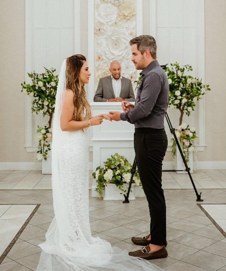 CasalSimone Mendes e Kaká Diniz  em momento especial trocando alianças em uma cerimônia elegante. Noiva veste vestido rendado branco com véu longo, enquanto noivo usa traje casual sofisticado. Decoração com flores brancas e folhagens destaca o charme dos casamentos de famosos 2025.
