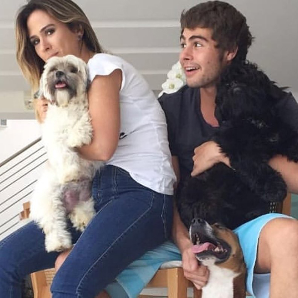Tata Werneck de blusa branca e calça jeans segurando cachorro branco, ao lado de Rafa Vitti segurando um cachorro preto e fazendo carinho em outro marrom 
