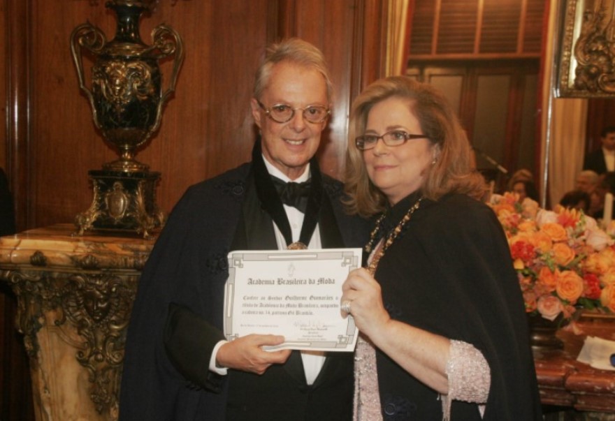 Foto de Guilherme Guimarães mais velho recebendo seu diploma de membro da Academia Brasileira da Moda das mãos de Hildegard Angel