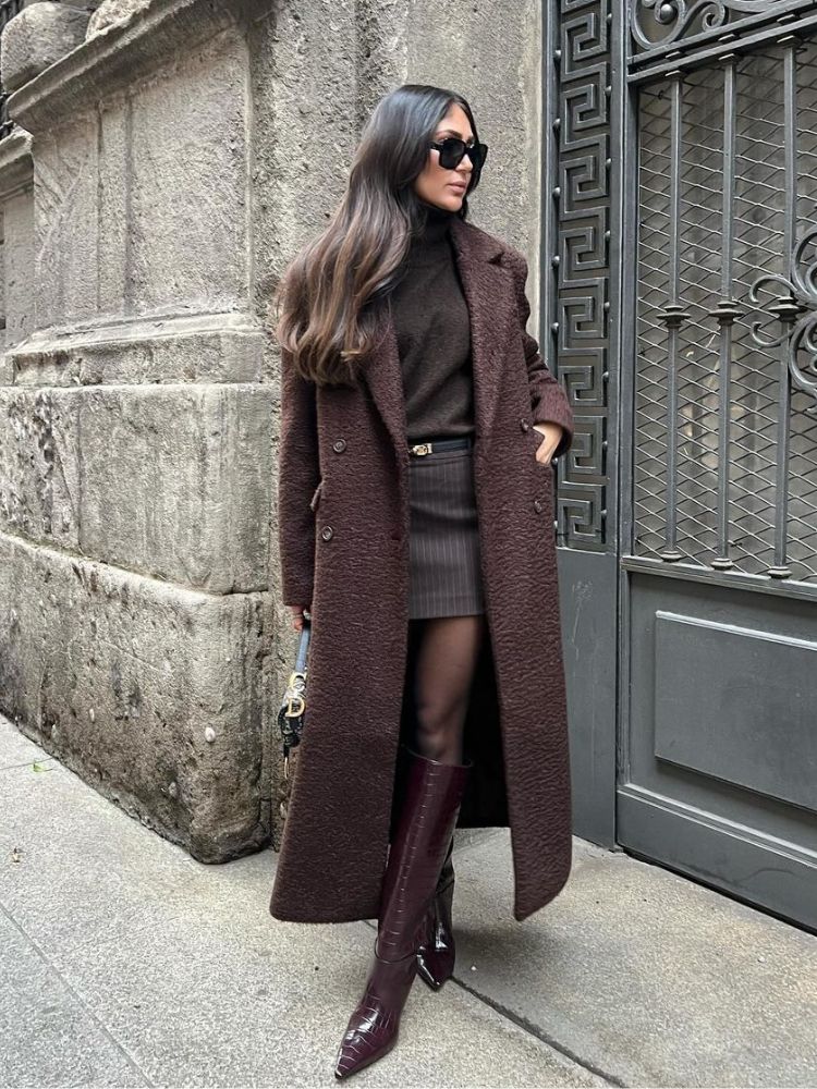 mulher usando sobretudo, suéter, saia, meia calça e bota, tudo parte de um look marrom