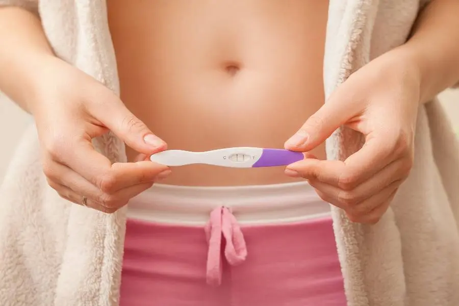 Mulher com teste positivo na frente da barriga.