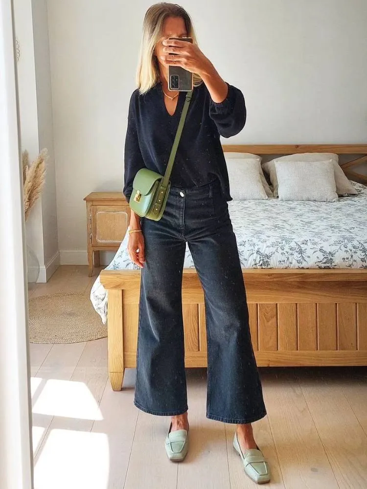 mulher com blusa preta, calça wide leg jeans e mocassim verde