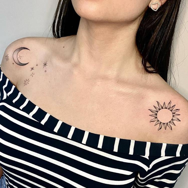 Mulher de pele clara e cabelo preto usando blusa de ombro a ombro branca e preta, com duas tatuagens, uma em cada ombro: uma de lua e outra de sol