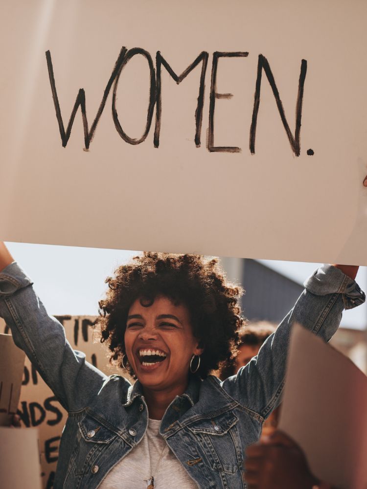 Mulher de pele negra segurando cartaz escrito "women"