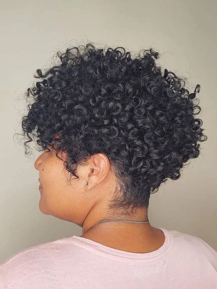 Mulher negra de perfil com cabelo cacheado curto em pixie repicado