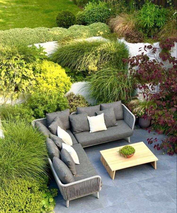 A imagem retrata um exuberante jardim florido, com uma variedade de plantas em tons vibrantes de roxo, lilás e verde. Um caminho sinuoso atravessa o cenário, rodeado por árvores altas, arbustos densos e flores coloridas, criando harmonia natural.