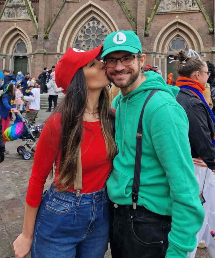 Fantasia de casal para o Halloween: Mário e Luigi. Ela usa blusa vermelha, boné vermelho e e calça jeans. Ele usa boné verde, moletom verde e calça 