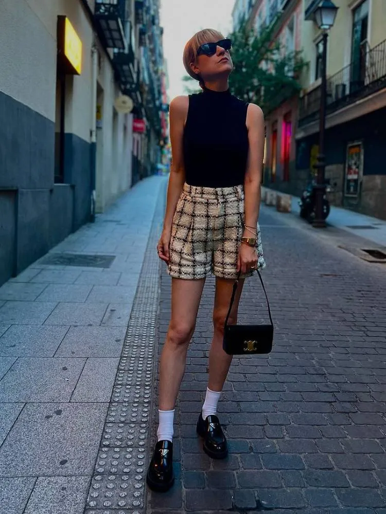 mulher usando regata preta de gola alta, short de tweed e mocassim preto