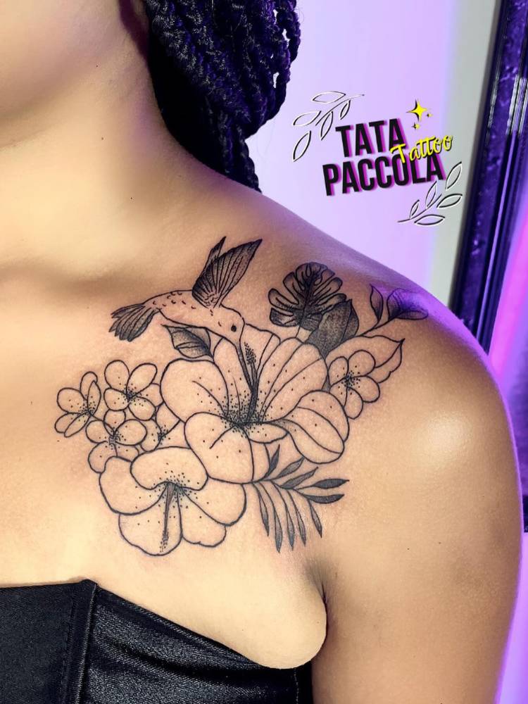 Mulher de pele morena com tatuagem de lírios, ramos e costela-de-adão sombreadas no ombro