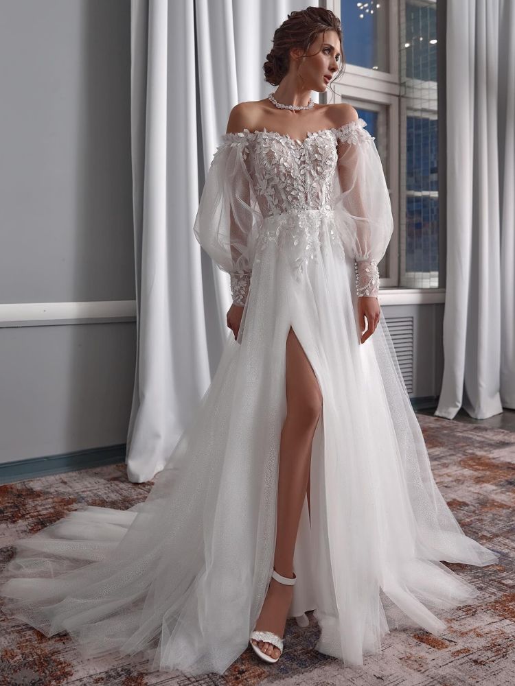 Mulher de pele clara usando vestido de noiva com fenda lateral, manga bufante transparente e aplicações de brilho no corselet. 