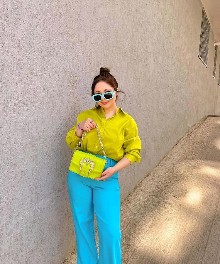 Mulher com camisa verde, calça azul, bolsa verde e óculos azul para torcer pelo Brasil