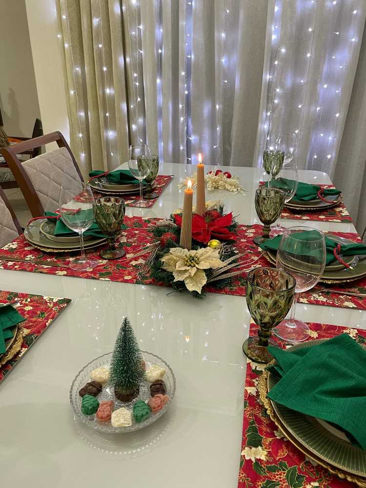Mesa posta com decorações natalinas, velas, mini árvore de Natal e jogo americano natalino.