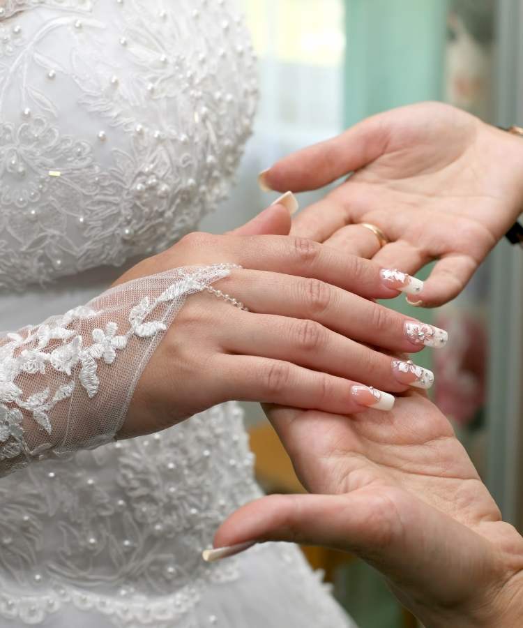 Mulher de pele clara usando vestido de noiva, luvas e unhas quadradas frandes, decoradas com flores brancas