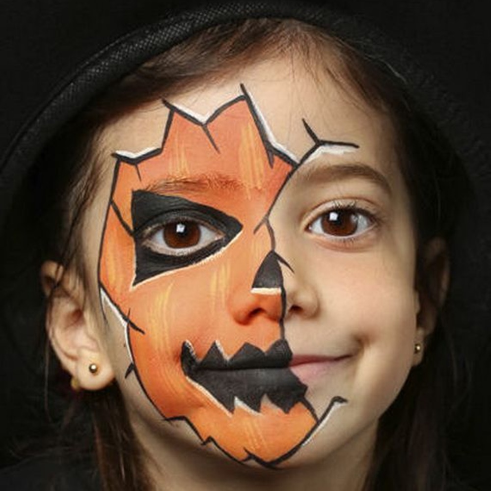 Criança com pintura de abóbora no rosto - Halloween em casa. Menina com pintura de abóbora.