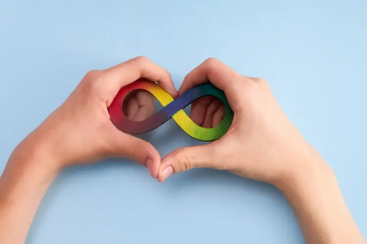 Pessoa de pele clara fazendo coração com as mãos sobre infinito colorido, símbolo da neurodivergência