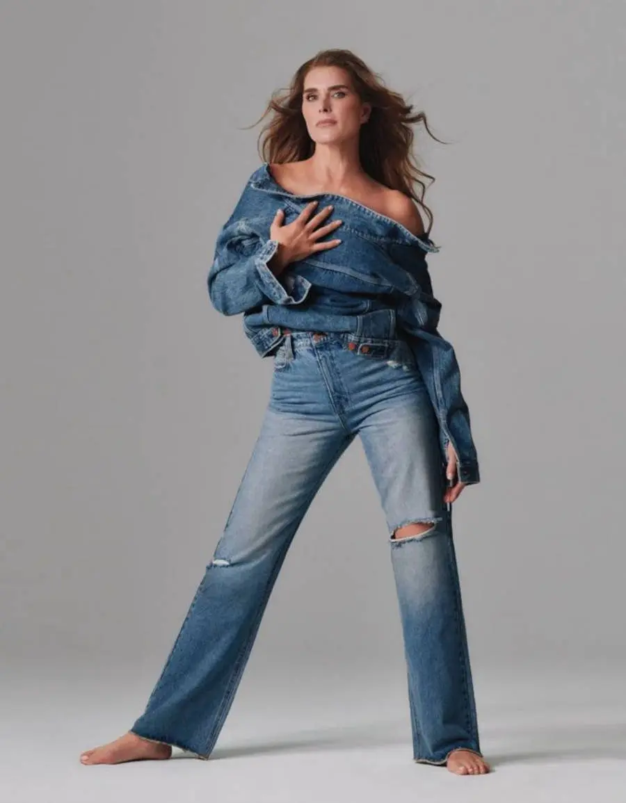 Imagem de Brooke Shields com calça jeans e segurando uma jaqueta jeans durante o photoshoot da marca Calvin Klein