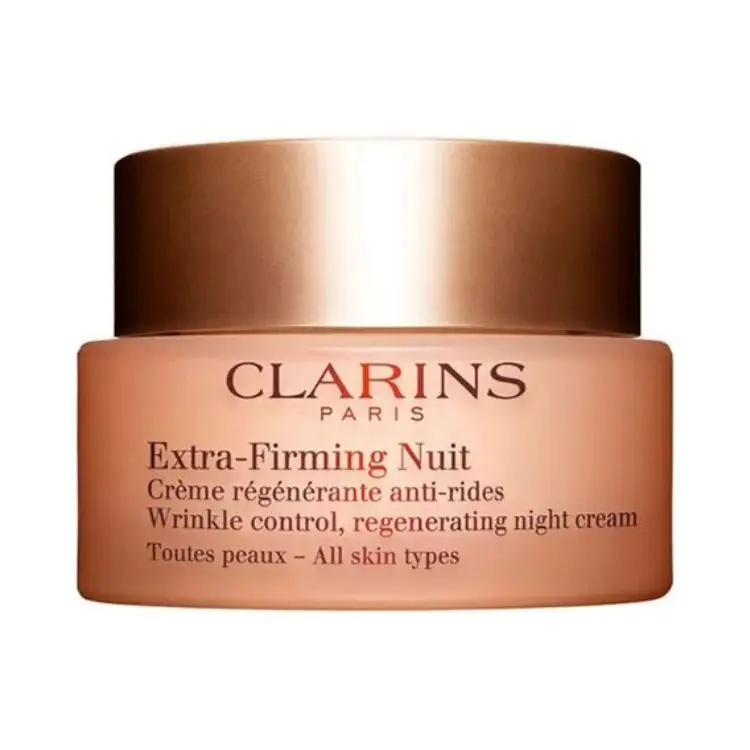 A imagem exibe um pote de creme Clarins Extra-Firming Nuit, um creme noturno regenerador anti-rugas. A embalagem é de cor pêssego, com tampa marrom acobreada, e é indicado para todos os tipos de pele. O texto no pote está em francês e inglês.


