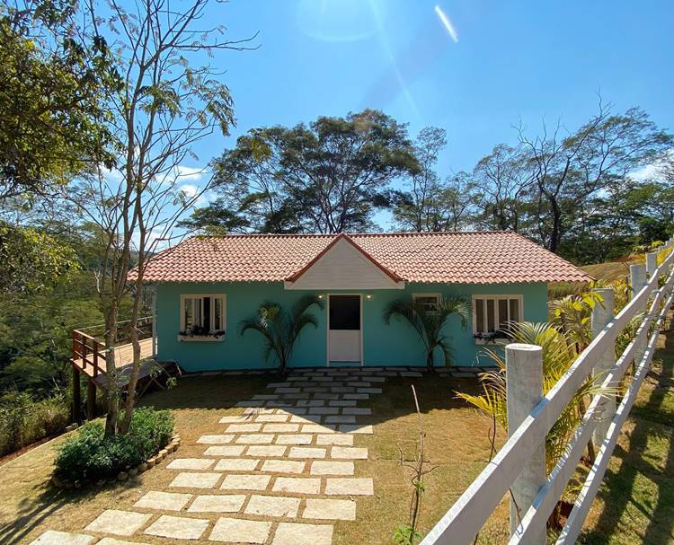 Imagem de fachada de casa simples azul com caminho em pedras retangulares posicionadas em gramado
