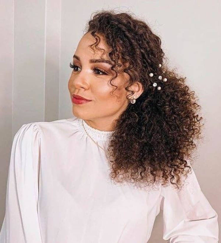 Mulher de pele morena com cabelo castanho cacheado com pérolas