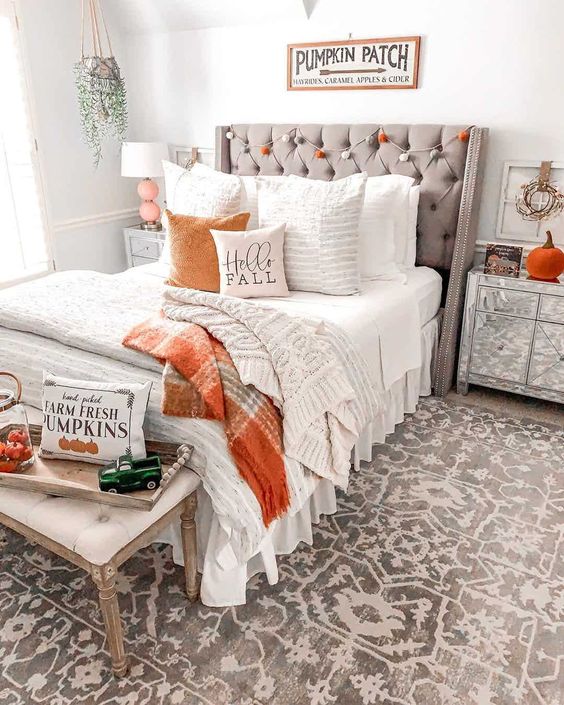 Quarto decorado para outono, com roupa de cama branca, manta e almofada laranja, além de abóboras 