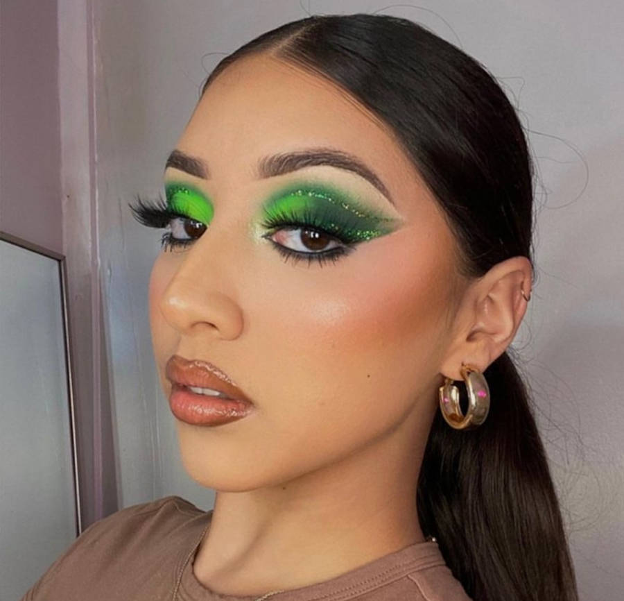 Mulher de pele clara com sombra verde, delineado verde e dourado e gloss marrom
