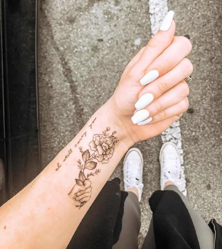 tatuagem no pulso de mão segurando rosa e frase 