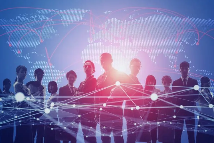 Grupo de profissionais em frente a um mapa mundi digital iluminado, com redes conectando pontos globais. Linhas brilhantes no primeiro plano representam conexão, colaboração e comunicação em um mundo globalizado e interconectado, destacando oportunidades em tempos de transformação.
