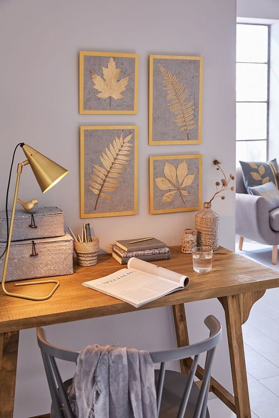 Home office azul com mesa de madeira, luminária e quadros de folhas secas 