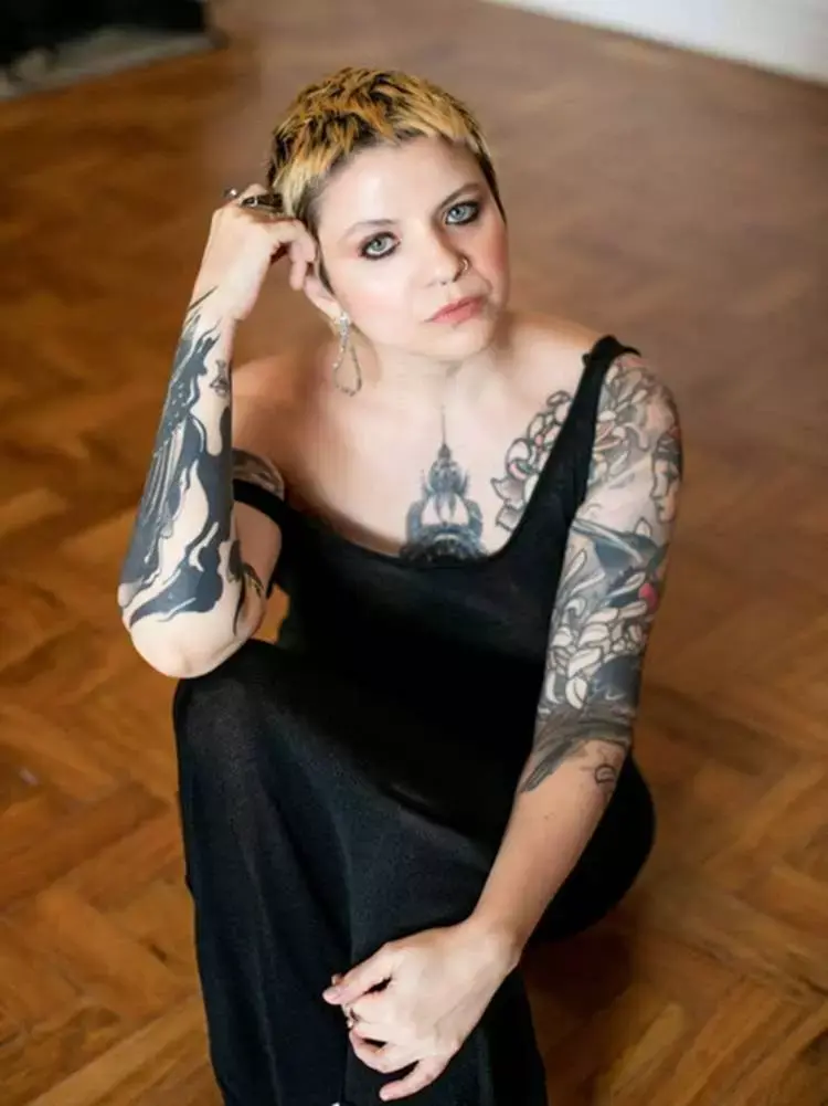 Mulher não-modelo com mais de 40 anos em ensaio fotográfico, usando vestido preto, sentada em chão de madeira
