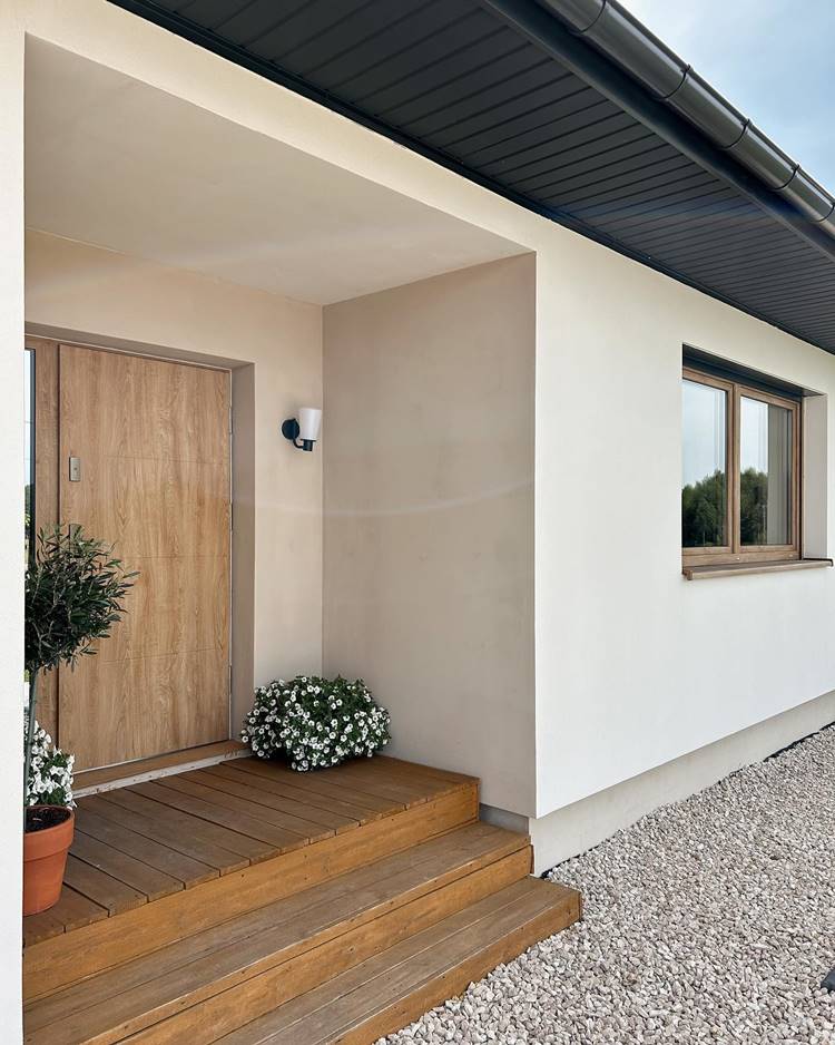 Imagem de fachada de casa simples e moderna. Cor branca, escada em madeira com flores brancas em vasos e luminária na parede da porta