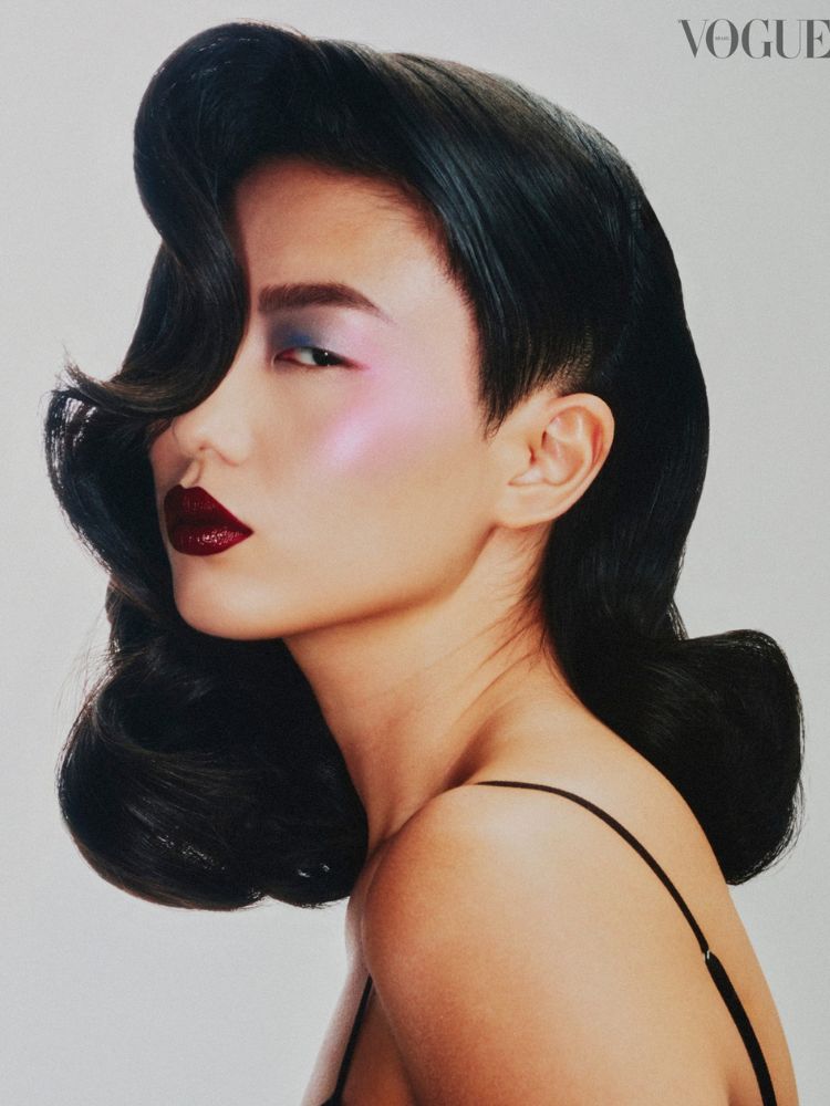 Mulher de origem asiática com cabelo modelado, batom vinho, sombra colorida e pele iluminada 