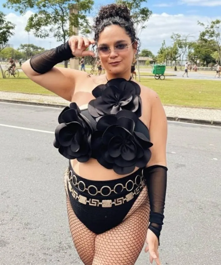 Foto de mulher usando look confortável de Carnaval: top de flor, hot pant, meia arrastão e sobreposição de cintos