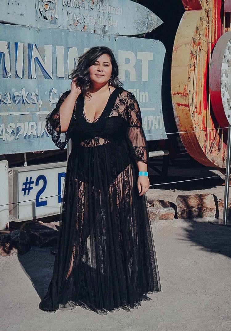 Mulher de pele clara com body preto por baixo de vestido transparente de renda preto