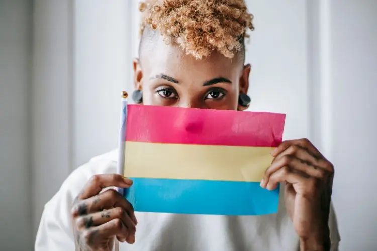 Pessoa de pele negra segurando pequena bandeira pansexual, com as cores rosa, amarela e azul