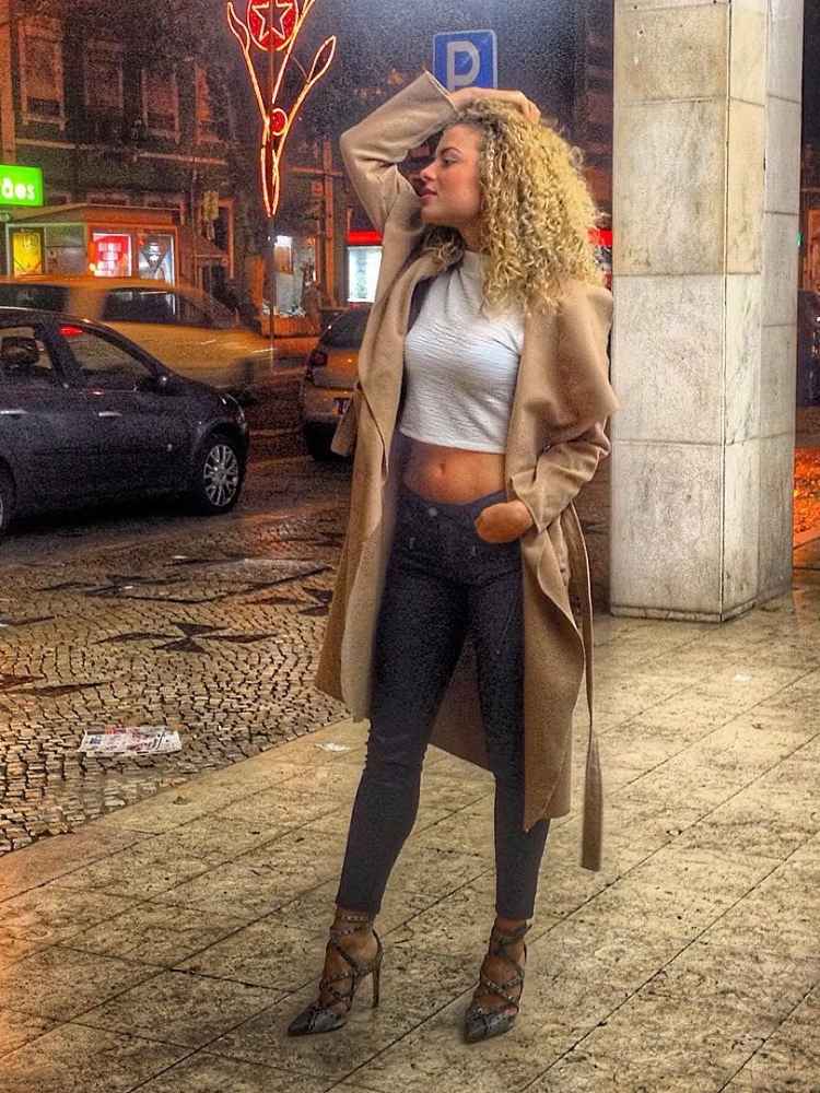 Larissa em 2015 usando cropped branco, calça skinny preta, sobretudo bege, na calçada em Portugal