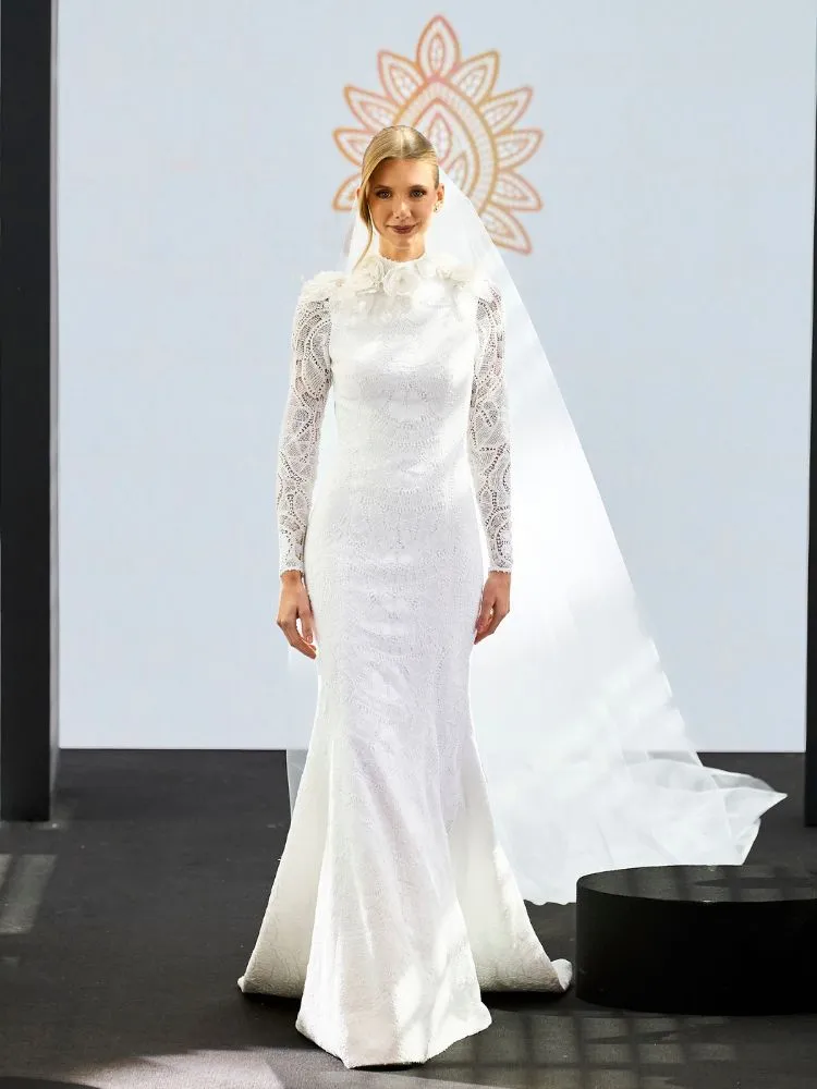 Bertha Bulhões com vestido de noiva longo, com manga de renda e véu longo e flores na região do pescoço