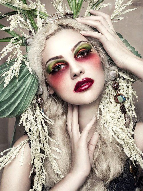 Mulher com maquiagem artística, com sombra verde e vermelha, batom vermelho, cabelo branco com plantas