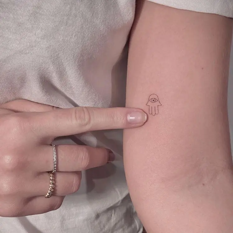 Tatuagem pequena, com design simples, de mão de Fátima em braço