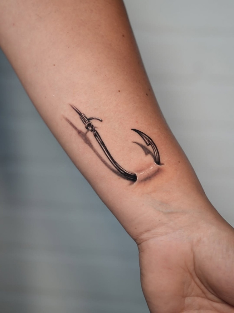 Tatuagem de anzol 3D entrando e saindo da pele do pulso 