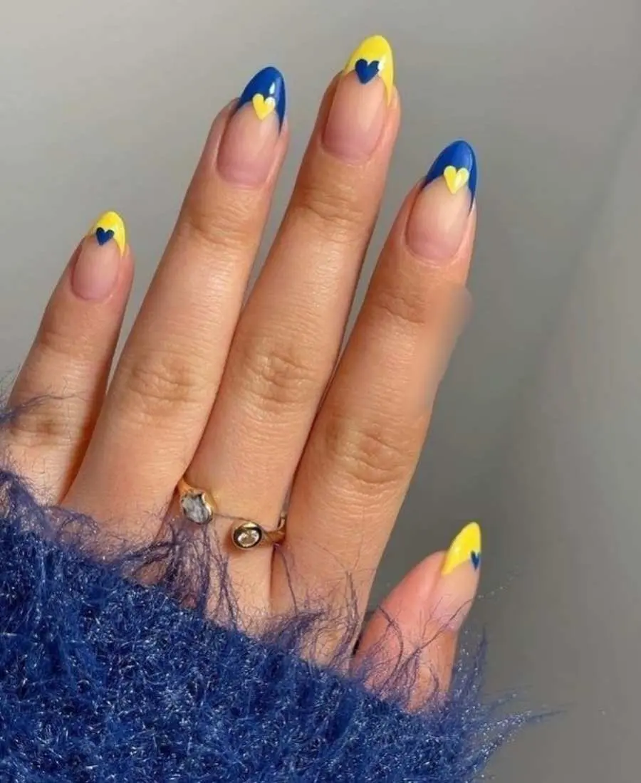 Imagem de mão com unhas decoradas para a Copa do Mundo 2022. Cores usadas: azul e amarelo. Polegar, médio e mínino, francesinha amarela com coração azul. Indicador e anelar, francesinha azul com coração amarelo. 